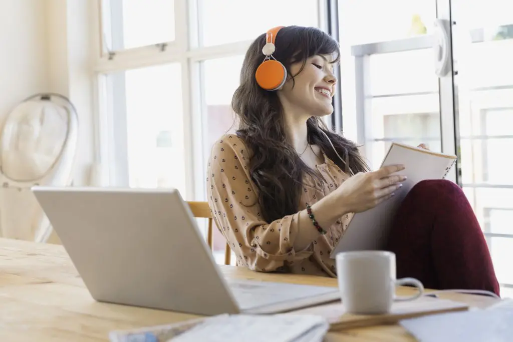 Woman with headphones and notebook at laptop